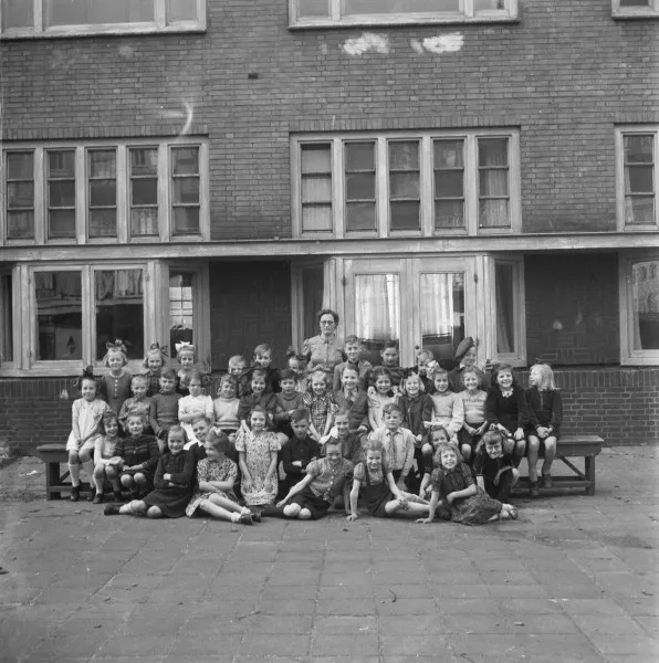 Afbeelding uit: april 1946. Klassenfoto op de binnenplaats. 39 kinderen en een onderwijzeres.