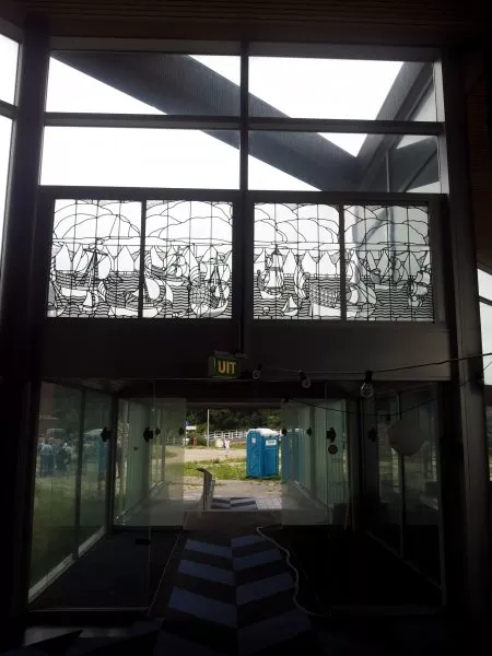 Afbeelding uit: september 2011. Decoratief raam boven de ingang aan het Overhoeksplein. Het door de firma Bogtman gemaakte raam kwam uit het IJ-paviljoen, een uitspanning aan het IJ die in de jaren 1970 plaats maakte voor de kantine van Shell. De huidige locatie van het raam is niet bekend.