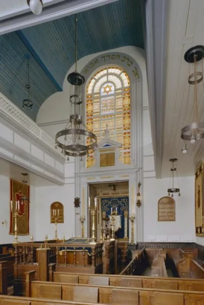 Afbeelding uit: 2001. Gebedsruimte van de synagoge met biema (verhoging voor het voorlezen van de Torah) en gebrandschilderd raam, gezien naar de Heilige Arke aan de oostkant van het gebouw.
