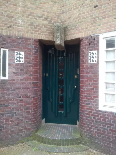 Afbeelding uit: augustus 2014. Willem Passtoorsstraat, portiek in een soort nis. Op de sluitsteen staat "Amsterd. Woningstichting Dageraad".