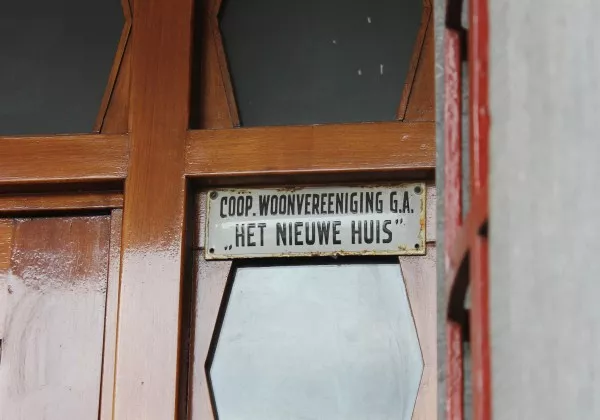 Afbeelding uit: september 2015. Naamplaatje van de "Coöp. Woonvereeniging G.A. Het Nieuwe Huis", de opdrachtgever en verhuurder van het gebouw.