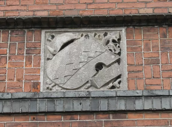 Afbeelding uit: maart 2016. Steen in de gevel aan de Rozengracht, met een schild met het wapen van Amsterdam. De steen zit in een laag met sierlijk metselwerk in een soort blokverband.