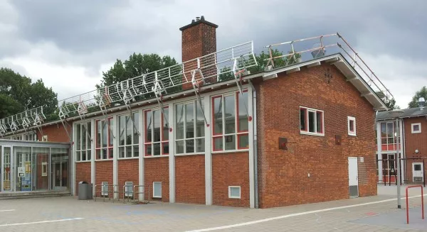 Afbeelding uit: juli 2016. De lagere vleugel, met onder meer de gymzaal. De hekken op het dak stonden er i.v.m. werkzaamheden.