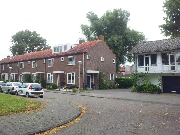 Afbeelding uit: juli 2016. De Bazelhof. Links woningen niet speciaal voor bejaarden (ook door Dudok ontworpen), rechts een deel van een rijtje met bovenwoningen, garages, bergingen en een winkel.