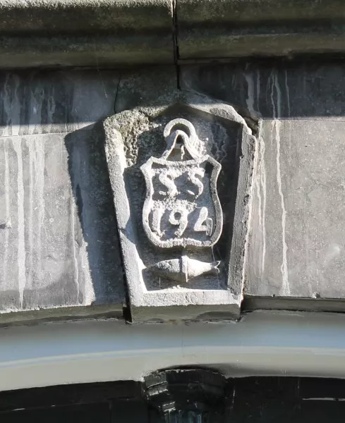 Afbeelding uit: oktober 2016. Sluitsteen boven de poort. SS 194 is het huisnummer volgens het systeem van 1853; de vis, een zalm, verwijst naar een oude naam van het adres.