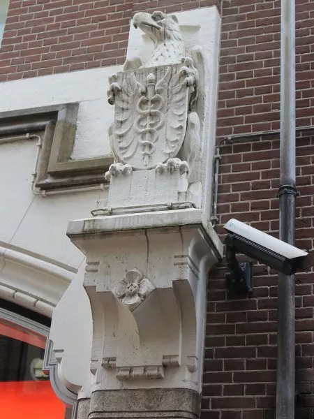 Afbeelding uit: februari 2017. Gevel Enge Kapelsteeg, bij de Kalverstraat. Een adelaar met een schild met daarop een symbool van de handel: de staf van Hermes met twee slangen.