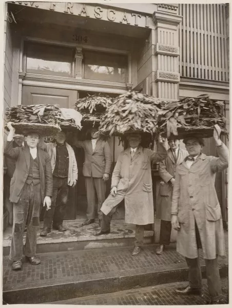 Afbeelding uit: maart 1929. Tabakshandelaren voor de ingang.
Bron afbeelding: SAA, bestand OSIM00006000503.