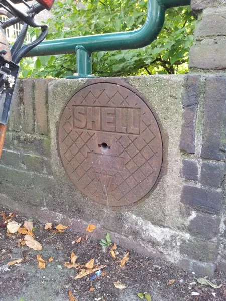 Afbeelding uit: augustus 2017. In het muurtje aan de Pijnackerstraat zit nog deze klep met opschrift Shell. Waarschijnlijk was het een vulpunt van de tank waarin de olie opgeslagen werd voor de verwarming van de kerk.