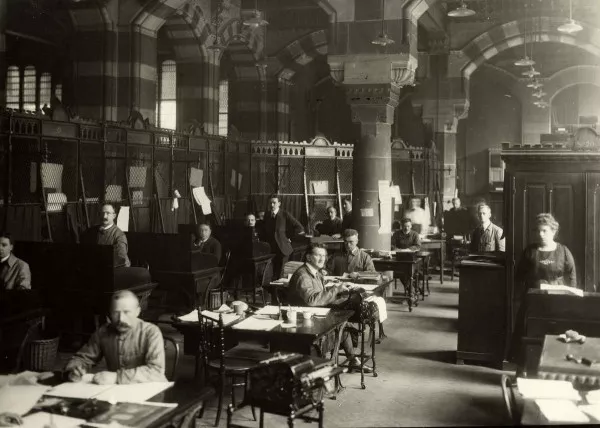 Afbeelding uit: circa 1921. Het grote lokaal van de afdeling postwissels met de loketten.