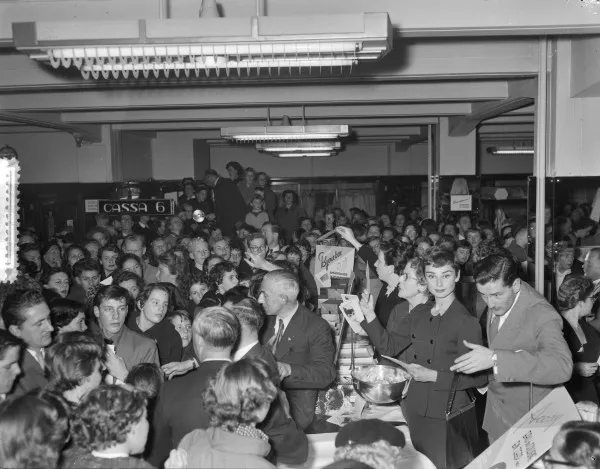 Afbeelding uit: november 1954. Mensen verdringen zich rond de kassa waar filmster Audrey Hepburn als verkoopster was ingehuurd. De actrice liep die dag ook mee als mannequin in een modeshow in de winkel.