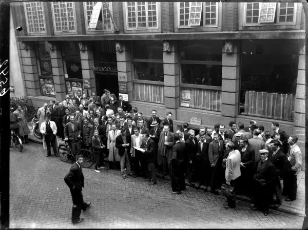 Afbeelding uit: september 1949. Een groep mannen voor de deur van het Arbeidsbureau. Het zijn werknemers van de in problemen verkerende stofzuigerfabriek EFA-Produka aan de Omval.