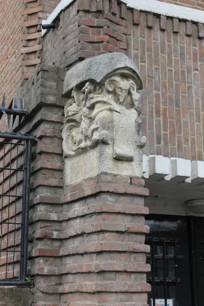 Afbeelding uit: december 2018. Een zandstenen sculptuur van Hildo Krop bij de linker ingang. Net als bij de andere ingang wordt een ram getoond die met een penneveer op een rol schrijft.