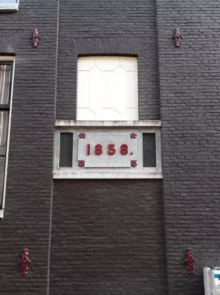 Afbeelding uit: februari 2019. Blind venster aan de Peperstraat met daaronder het bouwjaar 1858. Fraaie gegoten muurankers.