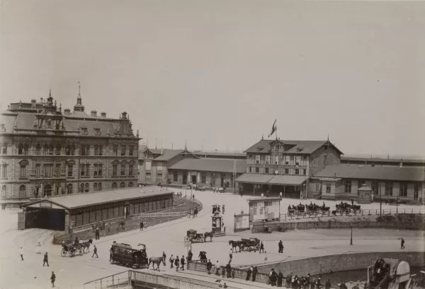 Afbeelding uit: circa 1885. Links, voor het kantoorgebouw, een tramremise van de AOM. Rechts het tijdelijke station Westerdok (1878-1889).
Bron afbeelding: SAA, bestand 010003012490.