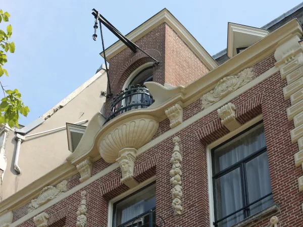 Afbeelding uit: augustus 2020. Bakstenen dakkapel. Balkonnetje met een schelp als console. Links en rechts ervan nog twee kapelletjes, met puntvormig uitkragende daken.