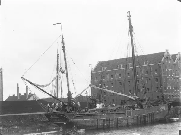 Afbeelding uit: 1895. Rechts twee van de pakhuizen in de oorspronkelijke staat. Het schip de voorgrond, met code AM12 op de boeg, was een Amsterdams vissersschip.
Bron afbeelding: SAA, bestand 010019000840.