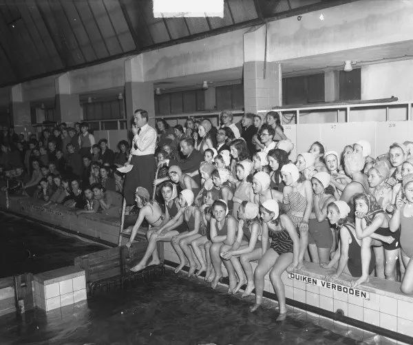 Afbeelding uit: december 1948. Schoolzwemwedstrijden. In het bad is een van de zuilen te zien die samen met hekken en schotten het 25-metergedeelte begrensde.