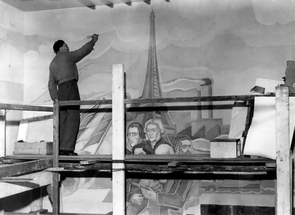 Afbeelding uit: februari 1950. Peter Alma werkend aan de muurschildering "Geschiedenis der Wetenschap". Te zien zijn onderwerpen uit de 19de eeuw: de Eiffeltoren, fabrieken; daarvoor Pasteur en Faraday, en verscholen achter de steiger Marx, Darwin en Hegel.