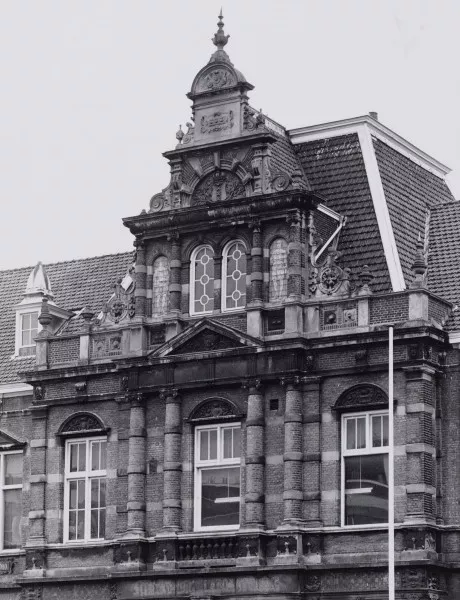 Afbeelding uit: april 1987. De geveltop aan de Roetersstraat. De torentjes die de top oorspronkelijk flankeerden waren toen al verdwenen.
Bron afbeelding: SAA, bestand 010122024397.