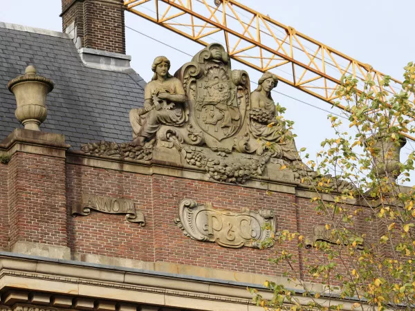 Afbeelding uit: oktober 2021. Tussen de vrouwelijke personificaties van cultuur en historie het wapenschild van Nederland. Op de banderollen staat "Anno Dᶦ", "P. & Co", en "MCMXVIII".