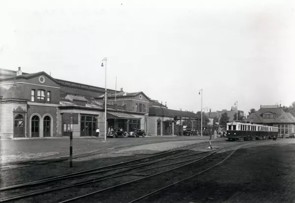 Afbeelding uit: 1934. Links het stationsgebouw van de spoorwegen, rechts een tram en het stationsgebouw van de Gooise Stoomtram. Collectie NS / Het Utrechts Archief, cat.nr 163666.