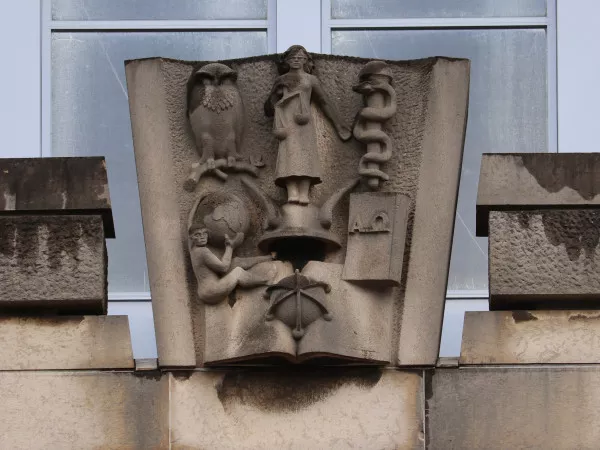 Afbeelding uit: januari 2022. Een van de plastieken op de dakrand, met symbolen van de zeven toenmalige faculteiten van de universiteit.
