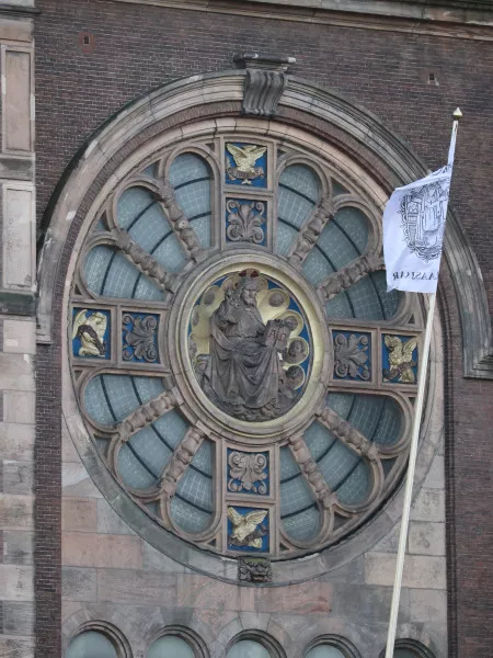 Afbeelding uit: januari 2022. Het rosetvenster boven de ingang. In het midden zit God ("de alfa en de omega"). De vier goudkleurige figuren zijn de symbolen van de vier apostelen: Johannes, Marcus, Lukas, Mattheus (van boven met de klok mee).