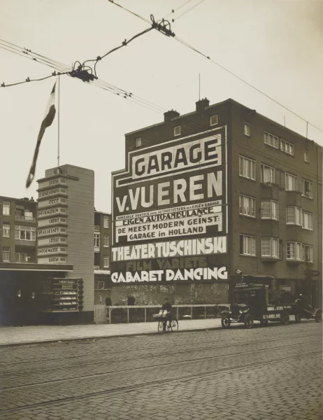 Afbeelding uit: 1928. Zijgevel. Het gemeentelijk reclametoezicht verordonneerde in 1928 dat Van Vueren de reclame voor Tuschinski moest verwijderen. Zoniet, dan zou de hele wand op zijn kosten worden overschilderd. (Rechts: de takelwagen van Van Vueren.)
