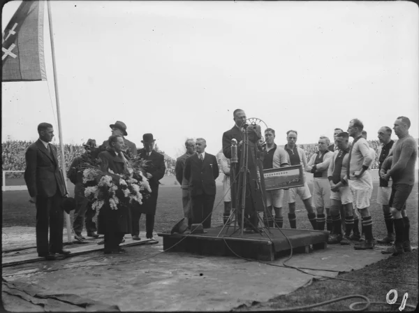 Afbeelding uit: december 1934. Architect Roodenburgh (links met krans) wordt bij de opening van het stadion toegesproken door Ajax-voorzitter Koolhaas.
Bron afbeelding: SAA, bestand ANWG00587000001.