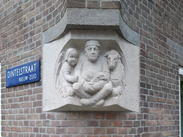 Afbeelding uit: december 2022. De sculptuur op de hoek Dintelstraat - Kennedylaan is van de hand van Jan Schultsz. Gemaakt in 1933, van graniet. Een zittende man met een kind en een lam aan zijn zijde. Tekst: "Zuid 1930".