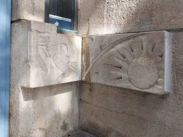 Afbeelding uit: september 2023. Decoratie rechts van de hoofdingang. Links een mannenhoofd, rechts een zon, als symbool van energie.