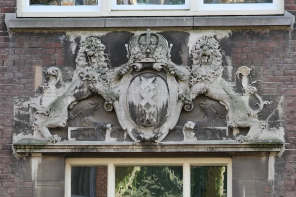 Afbeelding uit: december 2023. Twee leeuwen tonen een schild met het stadswapen en een keizerskroon. Bij hun poten de tekst "Anno MCMXI".