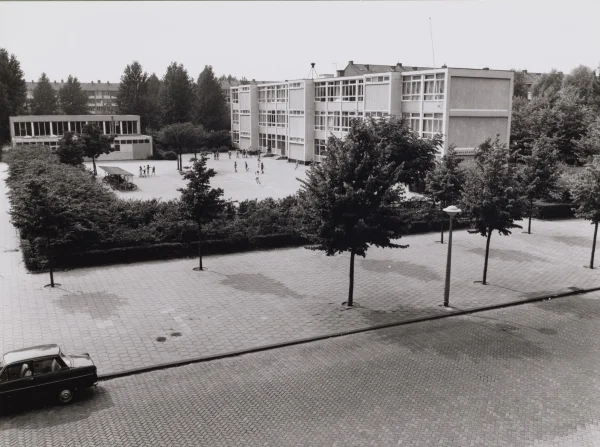 Afbeelding uit: augustus 1976. Het schoolplein in de jaren 1970. Op het dak staat een sirene voor luchtalarm.
Bron afbeelding: SAA, bestand B00000014626.