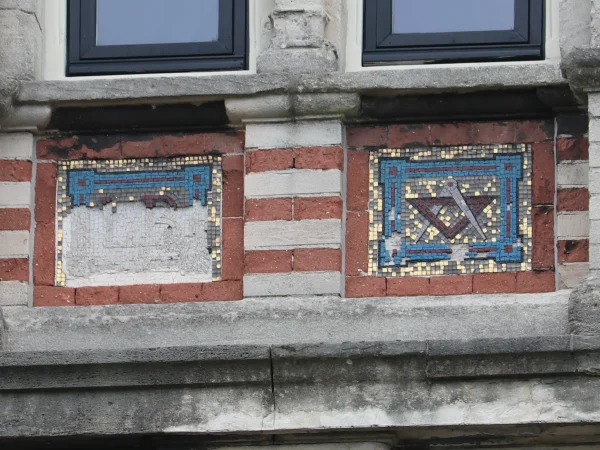 Afbeelding uit: augustus 2024. De mozaïeken die de signatuur van de architect vormen. Links de bijna geheel verdwenen letters LB, rechts het mozaïek met tekendriehoek en passer.