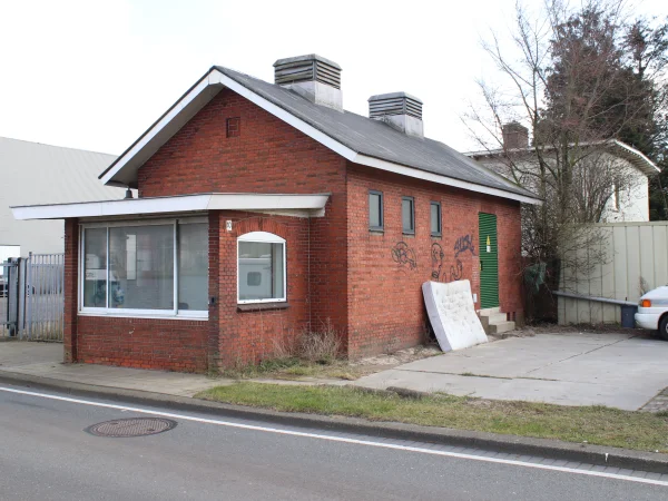 Afbeelding uit: maart 2025. Het gebouw met portiersloge en trafohuis. Op de achtergrond het voormalige kantoor.