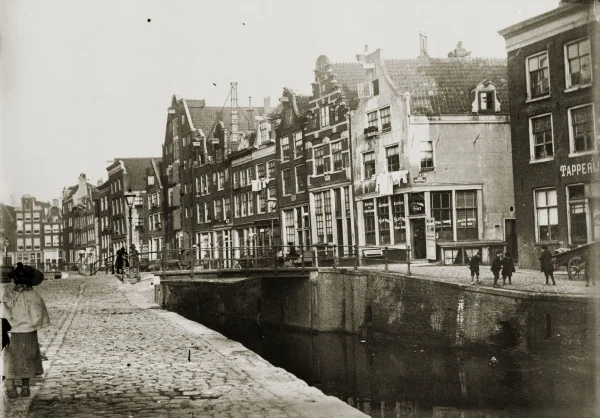 Afbeelding uit: 1898. Krom Boomssloot gezien naar de Recht Boomssloot, met rechts de Korte Keizersstraat en de voorganger van het huidige hoekpand.
Bron afbeelding: SAA, bestand 010104000220.
