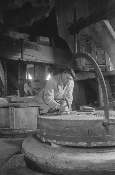 Afbeelding uit: mei 1962. Molenaar Schuurman werkt de groeven bij van een molensteen.