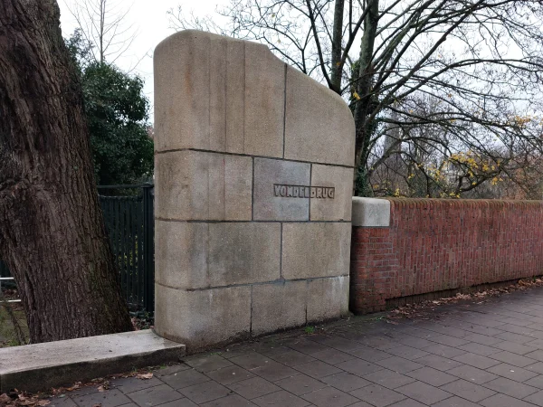 Afbeelding uit: december 2025. Massieve maar elegant afgewerkte markering van het begin van de brug aan de kant van de Van Baerlestraat.
