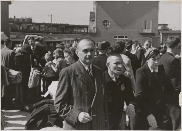 Afbeelding uit: mei 1943. Op 26 mei verzamelden zo'n 1700 Joden zich bij de kazerne voor vertrek naar kamp Westerbork, nadat de Duitsers ze verboden hadden nog langer in Amsterdam te wonen. Op de achtergrond de zijgevel van Ter Gouwstraat 18. Bron: beeldbankwo2.nl, beeldnr 96792.