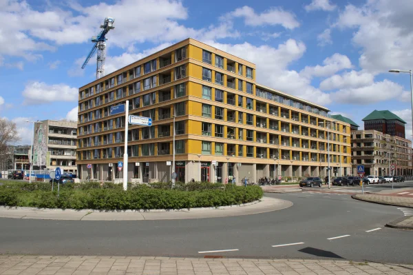 Afbeelding uit: april 2026. Gezien vanaf de Schipluidenlaan. Sinds 2024 gaat de school schuil achter gebouw Podium, een pand met 150 middenhuurwoningen ontworpen door bureau LEVS.