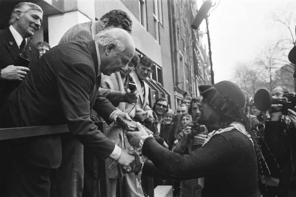 Afbeelding uit: februari 1977. Opening. Premier Den Uyl kreeg een boek van een man verkleed als Hugo de Groot. Die was net in de gracht gevallen, uit een daarboven bungelende boekenkist die door de blusboot van de brandweer open was gespoten. Het boek was deel 1 van Amsterdam in de 20e eeuw van Richter Roegholt.