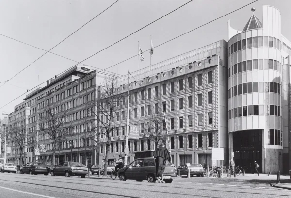 Afbeelding uit: april 1991. Vanaf 1987 stond aan de andere kant van de Lombardsteeg het pand van de Optiebeurs (architect: Cees Dam). Het had op de hoek een toren met een soort hoed die als groet aan de opmerkelijke kap van het gebouw van Van Arkel. Het postmoderne pand werd in 2012 verbouwd tot kantoor van NRC Handelsblad, waarbij de hoektoren verdween.
Bron afbeelding: Stadsarchief.