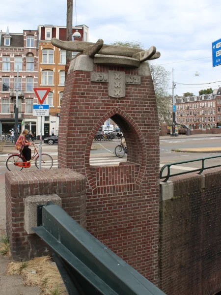 Afbeelding uit: augustus 2026. Kunstwerk bij de overgang naar de Rotterdammerbrug. Met het geplande maar niet gehaalde jaar van ingebruikname, 1952. Aan de andere kant heeft het een zitje.