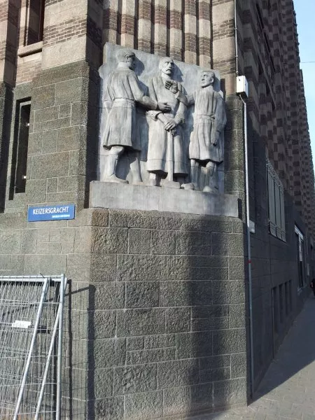 Afbeelding uit: november 2011. Beeldhouwwerk van J. Mendes da Costa op de hoek met de Keizersgracht. De man in het midden, met de voorhamer, stelt de Nijverheid voor; de twee figuren die handjeklap doen symboliseren de Handel.