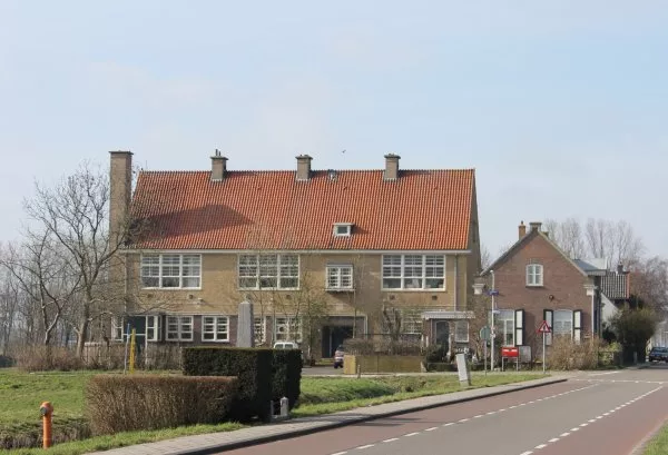 Afbeelding uit: maart 2012. Rechts de onderwijzerswoning. De obelisk op de voorgrond is het oorlogsmonument van Osdorp, aan de Osdorperweg.