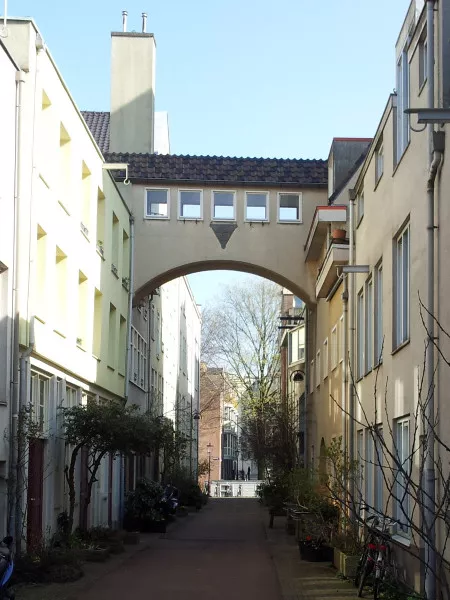 Afbeelding uit: maart 2012. De loopbrug over de Verversstraat verbindt sinds 1936 de twee delen van het complex: links dat aan de Groenburgwal, rechts dat aan de Zwanenburgwal. In het midden het driehoekige logo van de firma Leeuwenberg.