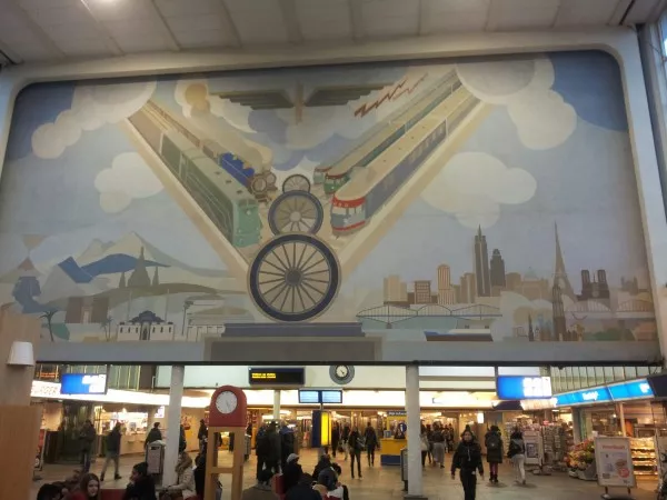 Afbeelding uit: november 2012. Een van de wandschilderingen van Peter Alma, 20 x 9 meter groot. Het (gevleugelde) wiel in het midden is het symbool van de spoorwegen. Links is de oude, oosterse wereld; rechts de moderne westerse, met Nederlandse en buitenlandse bestemmingen.
