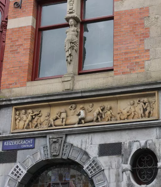 Afbeelding uit: mei 2013. Het beeldhouwwerk is gesigneerd met F.L.H. de Fernelmont. Als maker wordt echter in de literatuur E. Van den Bossche genoemd. Op de sluitsteen van de boog staat het monogram AB van de eigenaar van de winkel.