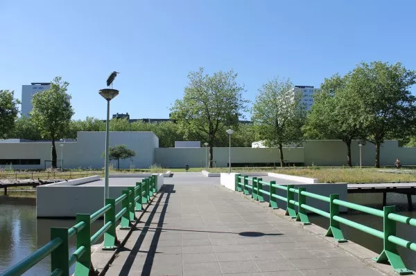 Afbeelding uit: juli 2013. Deze brug bij de Van Heenvlietlaan ligt er al sinds de jaren 1960. Architect was Dirk Sterenga van Publieke Werken. Het platform erachter is nieuw. Het verbindt twee houten vlonders langs de oever. Op de achtergrond de stadsdeelwerf (Claus & Gräber, 2008).